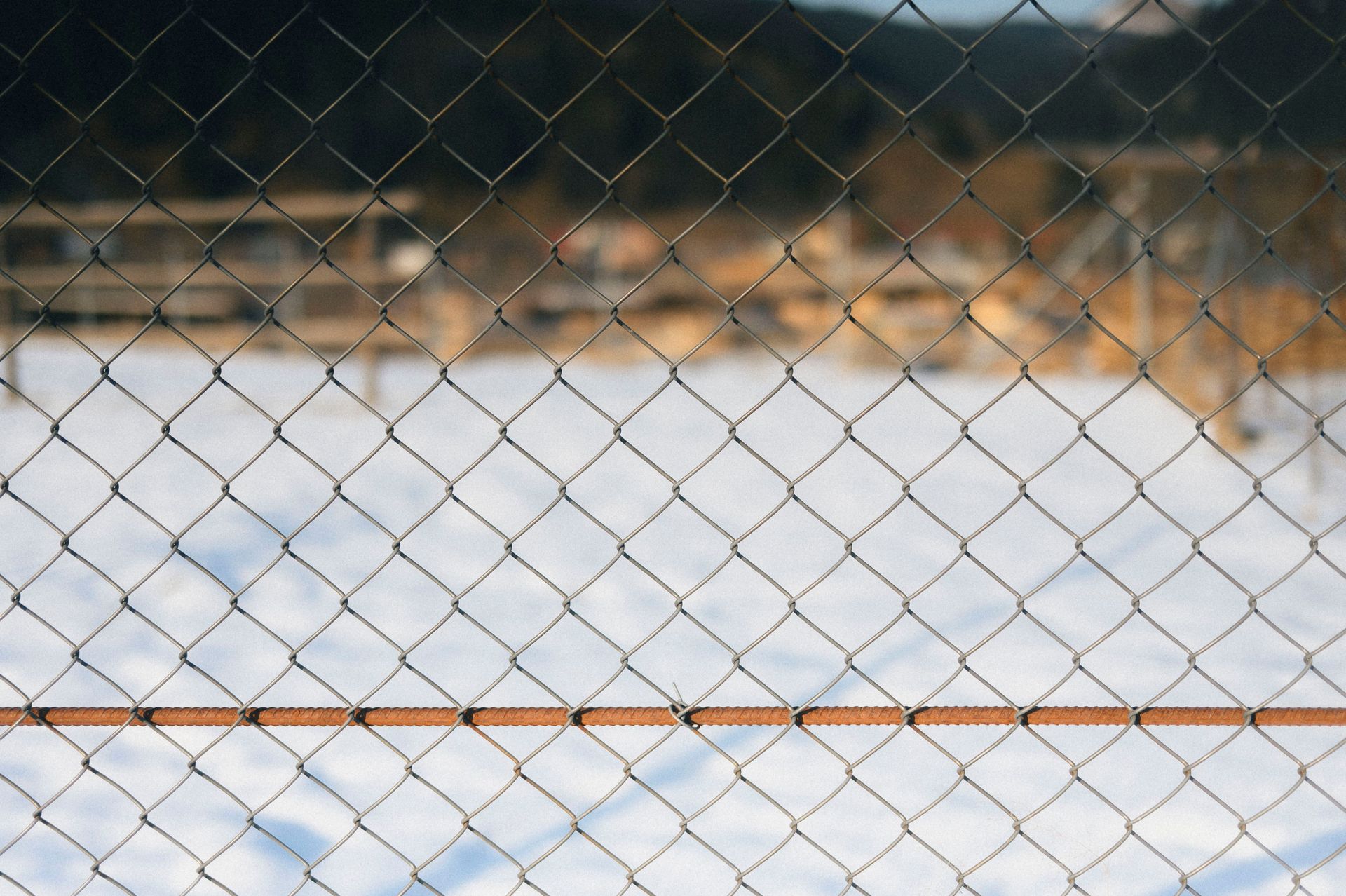 A chain link fence in sharp focus with a soft snowy backdrop, capturing a serene winter scene.